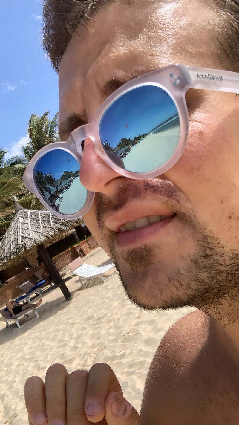 Nikita taking a beach selfie with sunglasses in a tropical setting